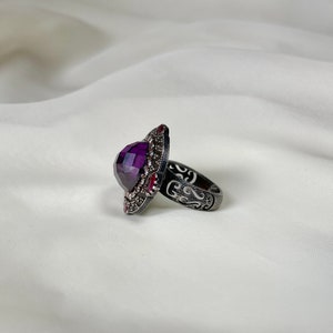 Puede incluir: Un anillo de plata con un dise&ntilde;o adornado y una gran piedra preciosa p&uacute;rpura facetada.