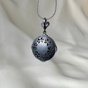 Puede incluir: Un collar de plata con un colgante redondo de dise&ntilde;o calado con un c&iacute;rculo de peque&ntilde;as flores. El colgante est&aacute; unido a una cadena de plata.