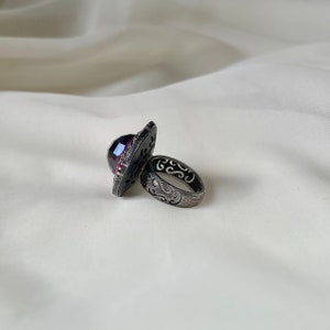 Puede incluir: Un anillo de plata con una gran piedra preciosa p&uacute;rpura facetada engastada en un dise&ntilde;o calado detallado. La banda del anillo tambi&eacute;n est&aacute; dise&ntilde;ada de forma intrincada con un acabado texturizado.