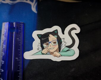 May include: A sticker featuring an anime-style character with cat ears, glasses, and a black and white hairstyle. The character is smiling and wearing a light green top. A blue ruler is next to the sticker.