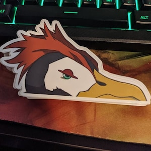 May include: A sticker featuring a cartoon bird with red, orange, and yellow feathers, a black beak, and a green eye. The bird's head is turned to the side, and its beak is slightly open.