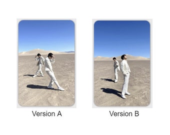 May include: Two people wearing white suits stand in a desert landscape. The person on the left is looking down, while the person on the right is looking up at the sky. The sky is blue and the sand is a light brown color. The image is labeled "Version A" and "Version B".