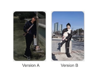 May include: Two images of a person wearing a black cap and black clothing. In the first image, the person is standing next to a pole and holding a bag. In the second image, the person is sitting on a stone bench and holding a small white dog.