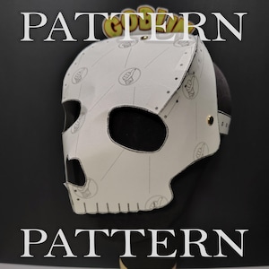 May include: A white skull-shaped mask featuring a repeating black line-art pattern of a hand giving a thumbs-up gesture. The mask has large eye and nose openings, visible metallic rivets along the side, and the word PATTERN printed in large white letters.