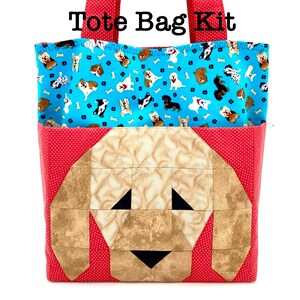 May include: A tote bag kit featuring a red fabric with white polka dots for the straps and base. The front displays a pieced fabric dog face in shades of tan and brown. The upper section is bright blue with a repeating pattern of various dog breeds.