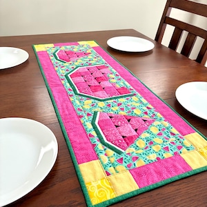 May include: A rectangular quilted table runner featuring three watermelon slice motifs. The design includes pink, yellow, and green fabric patches with a repeating pattern of small watermelons and lemons on a light blue background, finished with a green border.