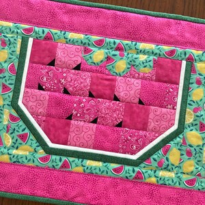 K&ouml;nnte beinhalten: Gesteppter Tischl&auml;ufer mit Wassermelonen-Design. Die Mitte zeigt eine rosa Wassermelonenscheibe mit wei&szlig;er Schale und schwarzen Kernen. Der L&auml;ufer hat einen rosa Rand und einen gr&uuml;n-t&uuml;rkisfarbenen Hintergrund mit Wassermelonen- und Zitronenmustern.