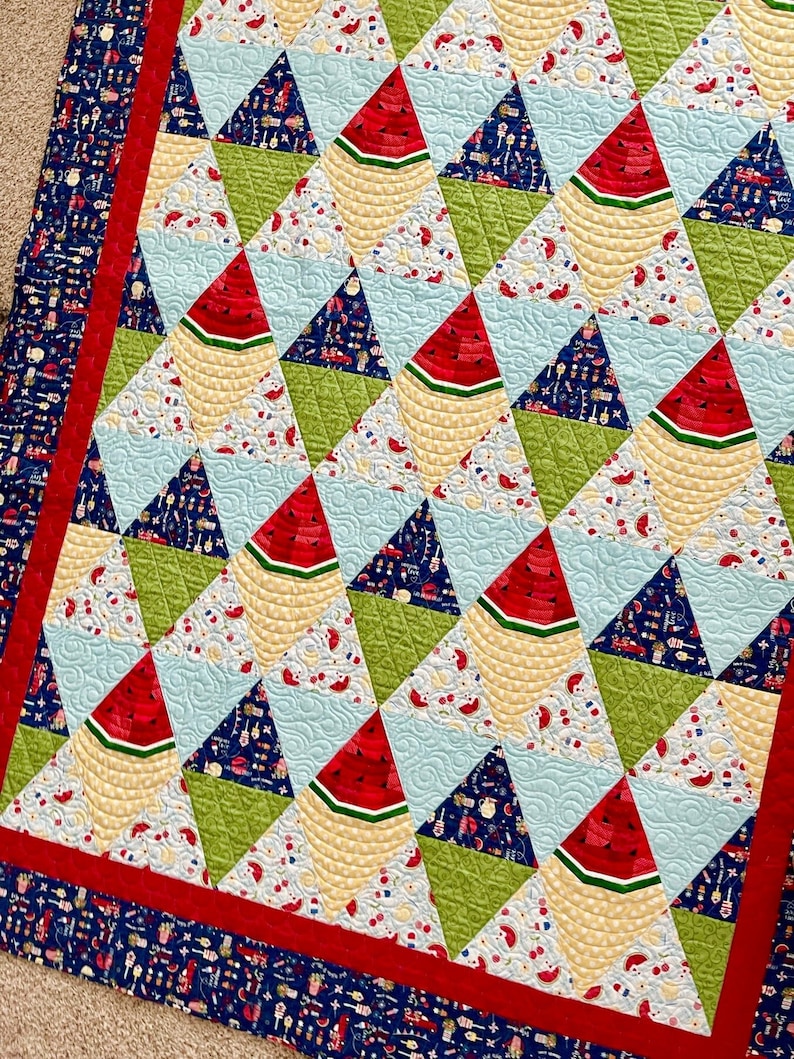 May include: A quilt with a patchwork design featuring watermelon slices, green, blue, and yellow triangles. The quilt has a red and blue border.
