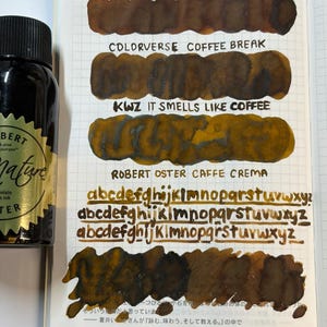 May include: A glass bottle of Robert Oster Signature fountain pen ink next to a notebook page featuring ink swatches and handwritten alphabet samples. The swatches are labeled Colorverse Coffee Break, KWZ It Smells Like Coffee, and Robert Oster Caffe Crema.