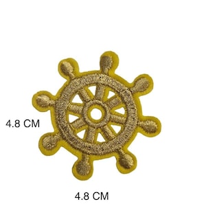 Może przedstawiać: Żółta naszywka z haftowanym złotym kołem sterowym statku, o średnicy 4,8 cm.