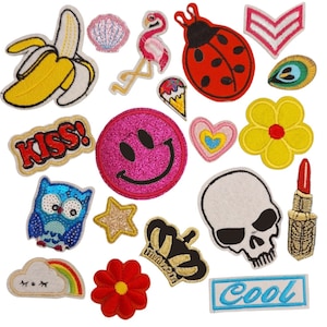 May include: A collection of colourful iron-on patches featuring various designs, including a banana, a seashell, a flamingo, a ladybug, a star, a crown, a skull, a flower, a rainbow, a smiley face, an owl, a lipstick, a heart, a cloud, and the words "Kiss!" and "Cool!"