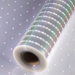 Puede incluir: Un rollo de papel de regalo transparente con un patrón de lunares blancos. El papel tiene un brillo iridiscente.