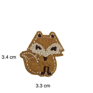 May include: A brown felt fox applique with white eyes and a brown nose. The fox is 3.3 cm wide and 3.4 cm tall.