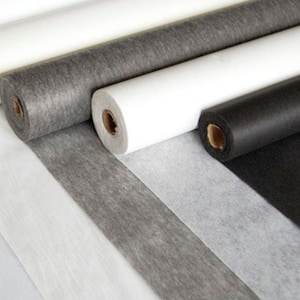 Pode incluir: Rolos de tecido de entretela branco, cinza e preto. O tecido é um material não tecido usado para estabilizar e fortalecer os tecidos.