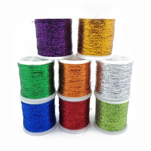 Può includere: Un set di otto bobine di filo metallico in vari colori, tra cui oro, argento, verde, rosso, blu, viola e arancio. Le bobine sono disposte a forma di piramide.
