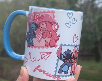 Op de afbeelding: Witte keramische mok met een blauw handvat en interieur. De mok heeft illustraties van een blauw en roze stripfiguurkoppel in verschillende poses, met de woorden "Love" en "Forever" in cursief. Harten en een papieren vliegtuigje zijn ook inbegrepen.