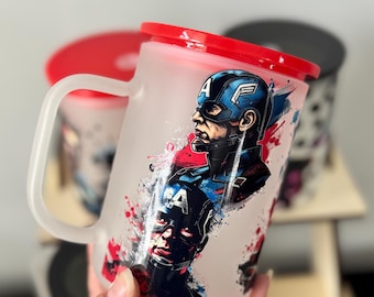 Op de afbeelding: Matglazen mok met Captain America-kunstwerk. De mok heeft een rode deksel en handvat. Het ontwerp bevat een portret van Captain America met rode, witte en blauwe accenten. Andere mokken zijn zichtbaar op de achtergrond.