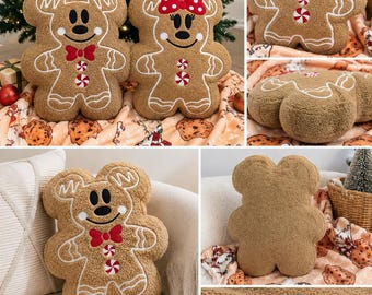 Op de afbeelding: Twee kussens van beige sherpastof in de vorm van peperkoekfiguren. De ene heeft een rode vlinderdas en twee pepermuntjes, de andere een rode strik met stippen en één pepermuntje. Beide hebben witte, geborduurde details van glazuur.