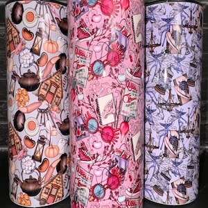 May include: Three stainless steel tumblers with different designs. The first tumbler has a light grey background with a pattern of brown beans, a teapot, a lantern, a house, and other objects. The second tumbler has a pink background with a pattern of red and blue glasses, a red shoe, and the words "The Quibbler". The third tumbler has a light purple background with a pattern of blue fairies with wings.