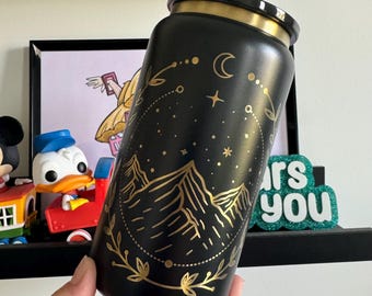 Op de afbeelding: Zwarte en gouden roestvrijstalen waterfles met een ontwerp van een bergketen, maan en sterren. Het ontwerp bevindt zich in een cirkel met een gouden bloemenpatroon rond de buitenkant.