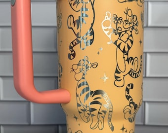 Op de afbeelding: Een hoge, lichtoranje geïsoleerde beker met een koraalkleurig handvat en deksel. De buitenkant heeft een herhalend patroon van zwarte lijntekeningen van Teigetje uit Winnie de Poeh, afgewisseld met kleine vierpuntige stervormen.