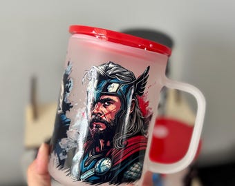 Op de afbeelding: Matglazen mok met een afbeelding van Thor, een rode deksel en handvat. De mok heeft een wit handvat en een rode deksel. De Thor-afbeelding is in tinten blauw, rood en wit.