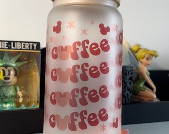 Op de afbeelding: Matglazen beker met een bamboe deksel. De beker heeft het woord "coffee" herhaald in een retro lettertype, met Mickey Mouse-hoofdvormen verwerkt in het ontwerp. Roze sterren en Mickey Mouse-vormen versieren het glas.