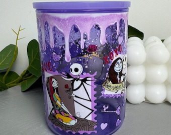 Op de afbeelding: Een paarse beker met een glinsterend druppelontwerp aan de bovenkant en afbeeldingen van Jack Skellington en Sally uit The Nightmare Before Christmas. De beker bevat de tekst XOXO en Simply Meant To Be, samen met hart- en sleutelpictogrammen.