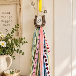 May include: A decorative wall hanging featuring a brown horseshoe with the text Lucky 7 and a four-leaf clover. It is suspended by a yellow ribbon with two dice attached to silver wires. A long tassel of multi-colored ribbons hangs below.