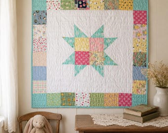 Op de afbeelding: Een vierkante patchwork quilt met een centrale achtpuntige ster van gele, roze en bloemrijke stoffen blokken op een witte achtergrond. De quilt is omrand door een kleurrijk kader van diverse stoffen vierkantjes met een turquoise bies.