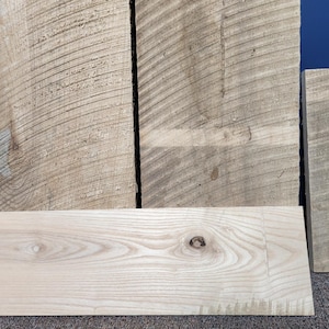 May include: Four pieces of wood with different grain patterns. The wood is light brown and has a natural finish. The wood is arranged in a vertical stack.