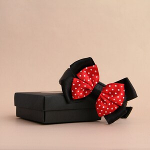 Könnte beinhalten: Eine rote Fliege mit weißen Punkten, gebunden und auf einem schwarzen Geschenkbox präsentiert.