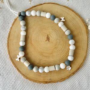 May include: A beaded accessory featuring a mix of round and cylindrical beads in shades of white, grey, and marble patterns. The strand includes two white bone-shaped charms and one white paw print charm, all strung on a white cord with a metal clasp.