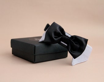 May include: A black and white bow tie with a white collar. The bow tie is made of satin and has a classic design. The bow tie is packaged in a black box.