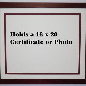 May include: A framed display with a burgundy-colored wooden frame and a white mat. The frame holds a white space with the text "Holds a 16 x 20 Certificate or Photo" in black. The frame is designed to display certificates or photos.