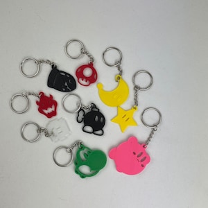 May include: A set of 10 colorful keychains featuring various Nintendo characters, including Mario, Luigi, Yoshi, and more. The keychains are made of plastic and have a silver metal ring.