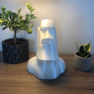 Op de afbeelding: Een wit 3D-geprint beeld van een Moai-hoofd, een traditioneel beeld van Paaseiland, op een houten oppervlak.