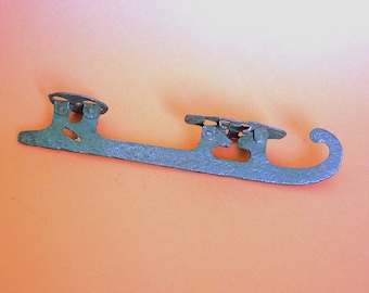 May include: A vintage metal ice skate with a blue-green patina. The skate has a curved blade and two metal straps with buckles.