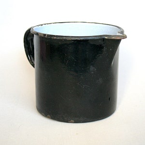 May include: Black enamelware pitcher with a white interior and a handle. The pitcher has a worn, vintage look.