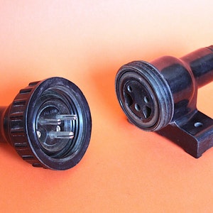 May include: Two black electrical plugs with three prongs. One plug is a standard plug and the other is a wall-mounted plug.