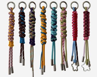 Puede incluir: Una colección de llaveros coloridos con diseños de cuerda trenzada. Cada llavero presenta un anillo plateado y una borla decorativa. Los llaveros son de varios colores, incluyendo amarillo, azul, verde y rojo. El texto "CESSY CHARM" y "KEYCHAIN" son visibles.