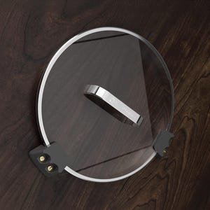 Könnte beinhalten: Ein transparenter Glasdeckel mit einem silbernen Griff und zwei schwarzen Clips an der Seite.