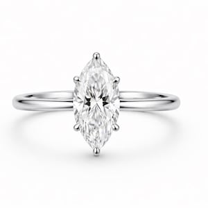 May include: A silver-toned ring featuring a single marquise-cut clear gemstone set in a six-prong setting. The band is smooth, polished, and slender, providing a clean and simple look that highlights the elongated shape of the central stone.