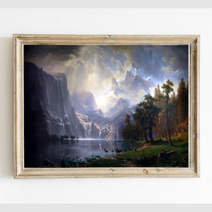 May include: A framed painting depicting a mountain landscape with a lake in the foreground. The sky is cloudy and the mountains are snow-capped. There are trees and a group of deer in the foreground.