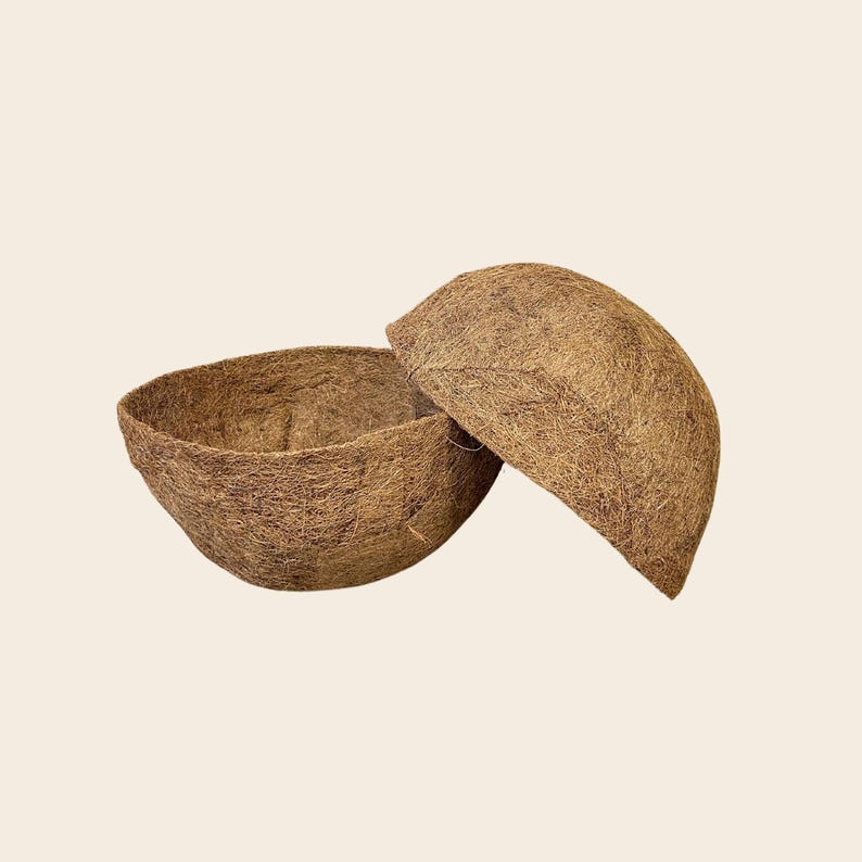 Op de afbeelding: Twee komvormige plantenbakken gemaakt van bruin, vezelig kokosvezelmateriaal. De ene plantenbak staat rechtop met een open binnenkant, terwijl de tweede plantenbak op zijn kant staat en de eerste gedeeltelijk overlapt om de afgeronde buitenkant te tonen.
