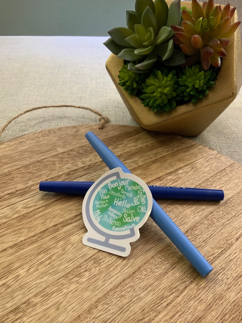 May include: A sticker of a globe with the word "Hello" in the centre and surrounded by greetings in different languages, including "Bonjour", "Merhaba", "Guten Tag", "Shalom", "Salve", and "Konnichiwa".