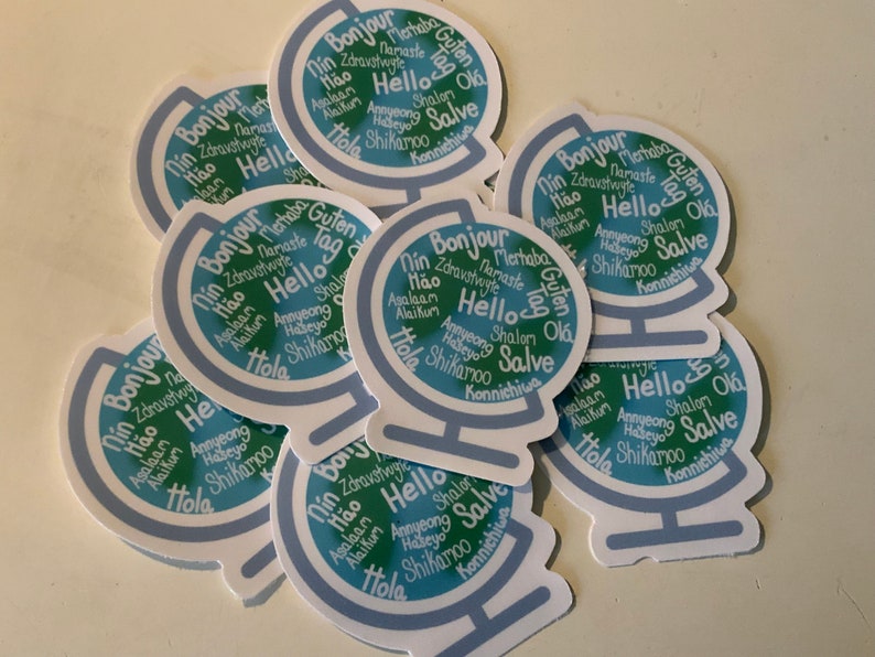 May include: A stack of blue and green globe stickers with the word "Hello" in multiple languages. The stickers are printed with a blue and green globe design and the words are arranged in a circle around the globe.