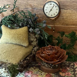 May include: A miniature fairy garden scene featuring a small clock, a rustic bench with a yellow pillow, and a decorative flower. The clock has a wooden frame and a white face with black numbers. The scene is set against a wooden backdrop.