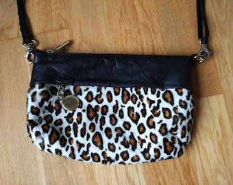 May include: A small black and white leopard print crossbody bag with a black leather flap and a silver zipper. The bag has a silver chain strap and a silver charm.