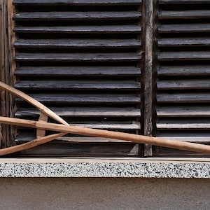 Puede incluir: Un tenedor de heno de madera con tres dientes, descansando en un alféizar de ventana. El tenedor está hecho de madera natural y tiene un mango largo.